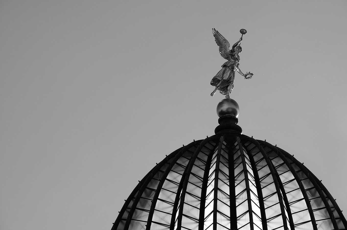 Black and white photo in Dresden, Germany. Glass dome with a golden angel on top, lit up from the sun shining from behind at sunset.