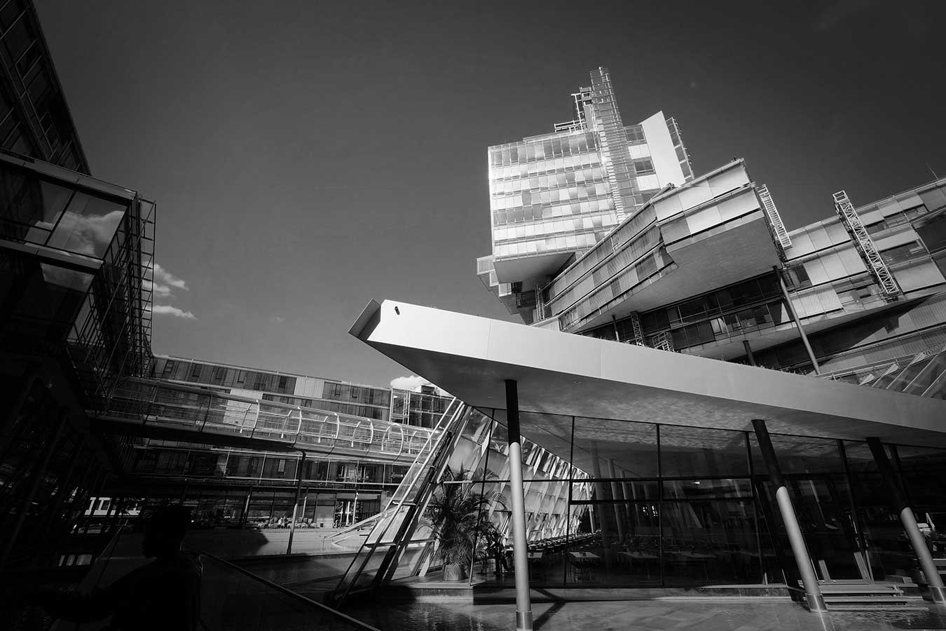 Black and white photo in Hannover, Germany. An angular, futuristic glass-covered building rises up from a spare courtyard.