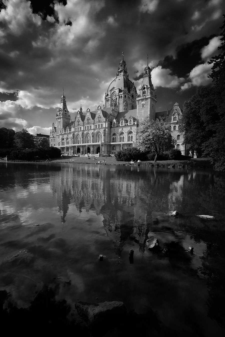 Black and white photo in Hannover, Germany. The town hall is reflected over a lake in the foreground, with looming clouds above.