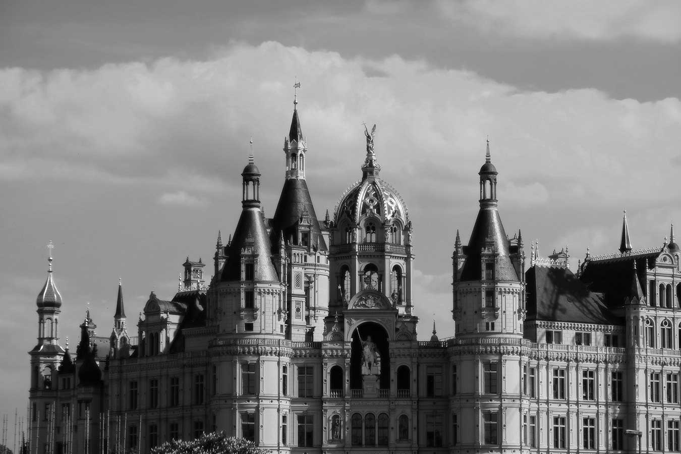 Black and white photo in Schwerin, Germany, showing the exterior of the Schwerin castle at sunset. Lots of towers and vertical elements.